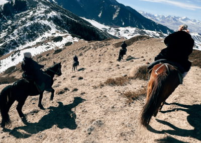 Eine bergige Landschaft, es sind drei Pferde mit ihren Reitern zu sehen.